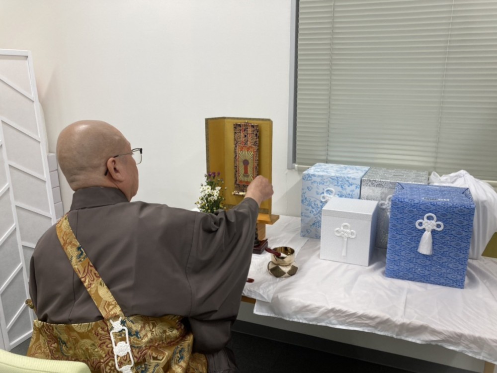 ライフジェムの事務所の一角で僧侶が読経し、ペットの骨壺の供養を行っている様子。供養台には骨壺が置かれている。