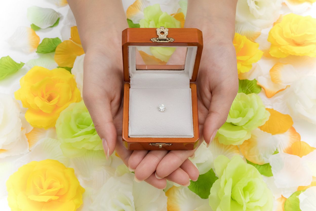 黄色と白の花々に囲まれ、両手で大切に捧げられた木箱。その中で一粒のメモリアルダイヤモンドが清らかに輝く。